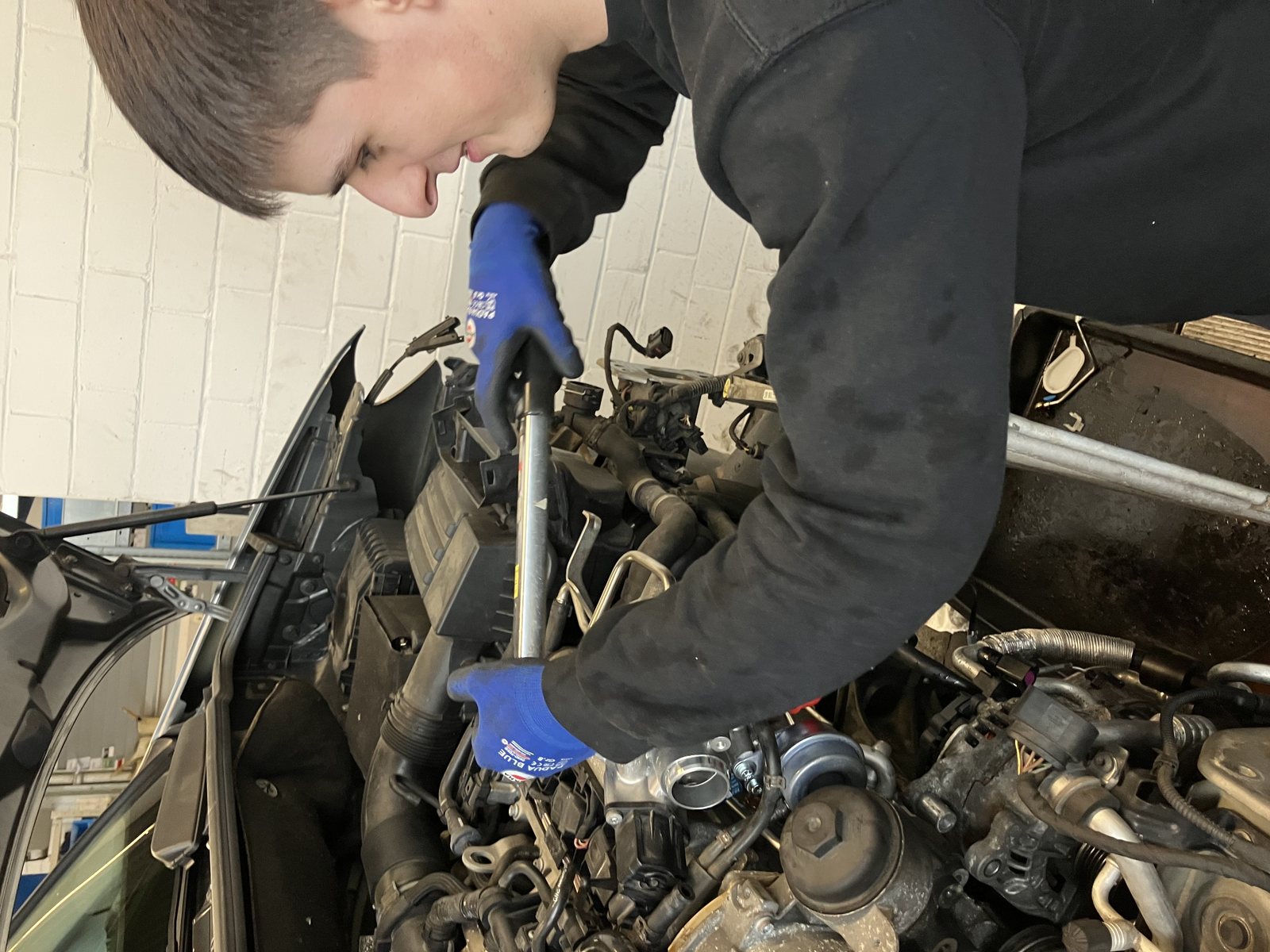 Kfz-Mechatroniker bei Arbeiten am geöffneten Motorraum